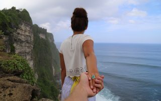 woman facing ocean view while holding partners hand